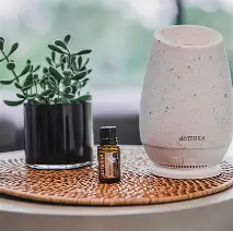 A ceramic ultrasonic diffuser releasing mist beside a small amber lavender oil bottle
